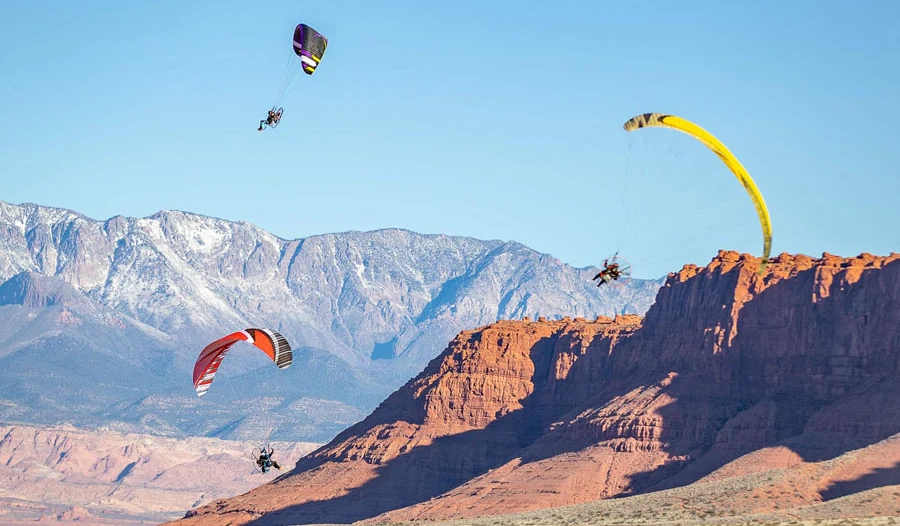 Three powered paragliders flying near red cliffs and snow-capped mountains in Southern Utah